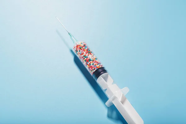 Syringe filled with colorful nano balls on a light blue background. Innovative medical concept of a cure for viruses and diseases. Gene modification