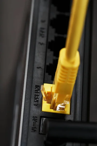 A yellow patch cord is inserted into the Wi-Fi port of the router to access the Internet. Internet connection via a wire with a router. Macro, close-up