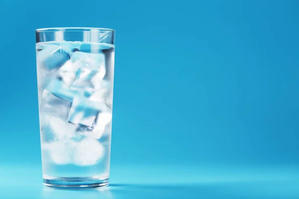 A glass with ice and clean water on a blue background. Free space, an icy drink in the sultry heat