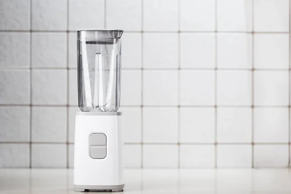 Empty electric blender in the kitchen for cocktails and healthy food. White blender on the table with light kitchen tiles. Minimal concept, copy space.