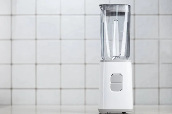 Empty electric blender in the kitchen for cocktails and healthy food. White blender on the table with light kitchen tiles. Minimal concept, copy space.