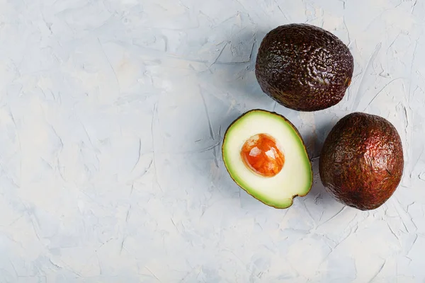 Sliced and whole organic Hass avocado on a gray background. A source of essential fats, vitamins, trace elements, beta-carotene and omega-3 fatty acids. Healthy food, diet. copy space