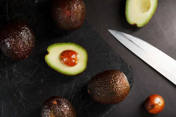 Sliced and whole organic avocado Hass with a knife on a black background. A source of essential fats, vitamins, trace elements, beta-carotene and omega-3 fatty acids.