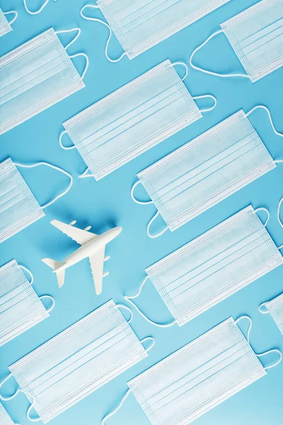 White airplane around protective masks on a blue background. The concept of the ban on flights and the mask mode, the threat of the spread of the virus. Top view