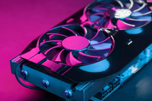Gaming graphics card with neon magenta-cyan illumination and high-speed fans. Video chip for mining and powerful games in the cyberpunk concept. Selective Focus