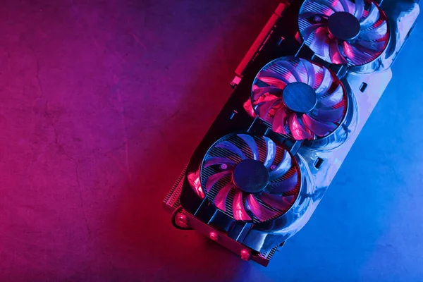 Gaming graphics card with neon magenta-cyan illumination and high-speed fans. Video chip for mining and powerful games in the cyberpunk concept.