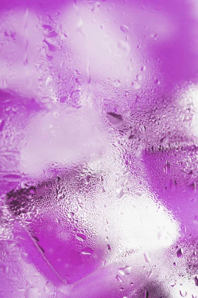 Ice cubes in a glass with refreshing ice water on a pink background. Close-up
