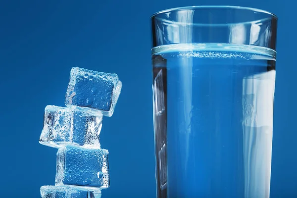 Ice cubes tower with a glass of cold and clean water on a blue background. Free space