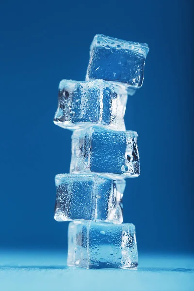 Frosty ice cubes in the form of a tower on a blue background. Water droplets, free space