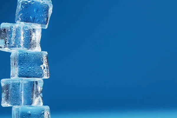 Ice cubes with water drops tower in a row on a blue background.