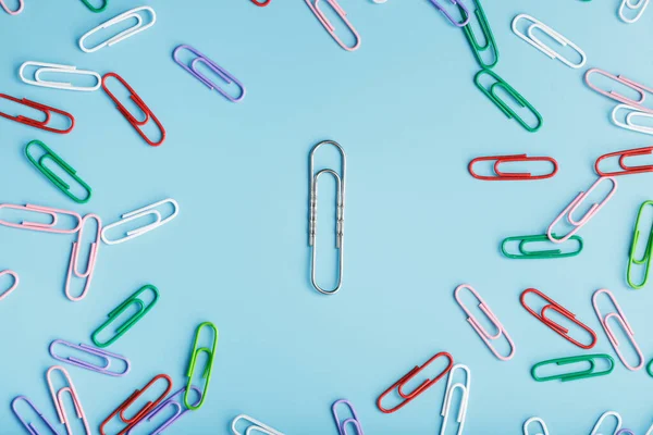 A large paper clip surrounded by small colored paper clips on a blue background.