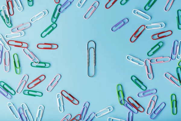A large paper clip surrounded by small colored paper clips on a blue background.
