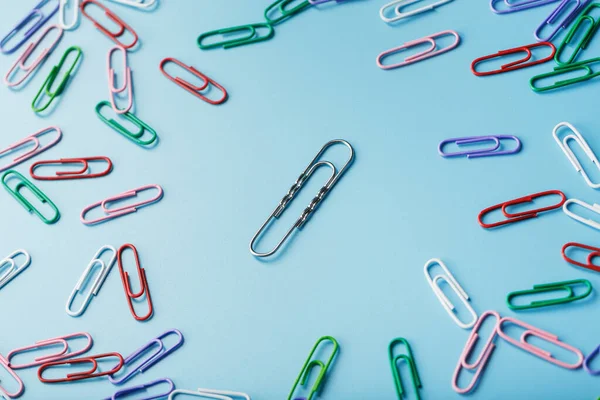 A large paper clip surrounded by small colored paper clips on a blue background