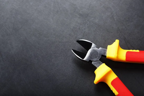 Pliers are a cutting tool with a red handle on a black background. Free space, top view