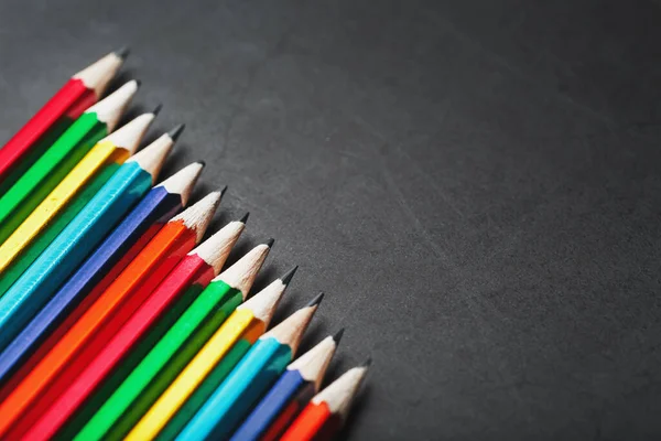 A set of colorful pencils on a textured dark background.