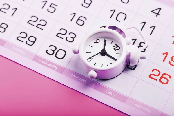 White alarm clock and calendar on a pink desktop background. Women\'s Days
