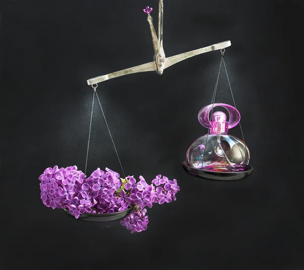 Natural and lilacs perfume bottle on opposing the scales. — Stock Photo, Image