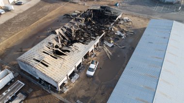 Yanan bir binanın önünde beyaz bir araba park edilmiş. Araba binanın önünde park edilmişti. Etrafı kül ve molozlarla çevriliydi. Sahne kaotik ve tehlikeli.