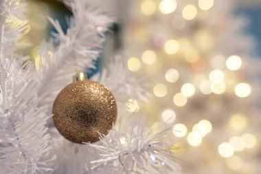 Beyaz bir ağacın üzerinde parlak altın bir Noel süsü ve arka planda da parlak bokeh ışıkları var. Minimum, zarif bir tatil. Kartlar ve tasarım planları için mükemmel..