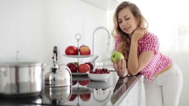 Κορίτσι στην κουζίνα κρατώντας πράσινο μήλο — Αρχείο Βίντεο