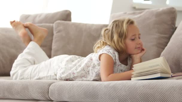 Tjej på soffan läser en bok — Stockvideo