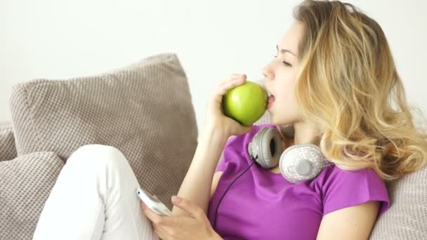 Женщина на диване ест яблоко — стоковое видео