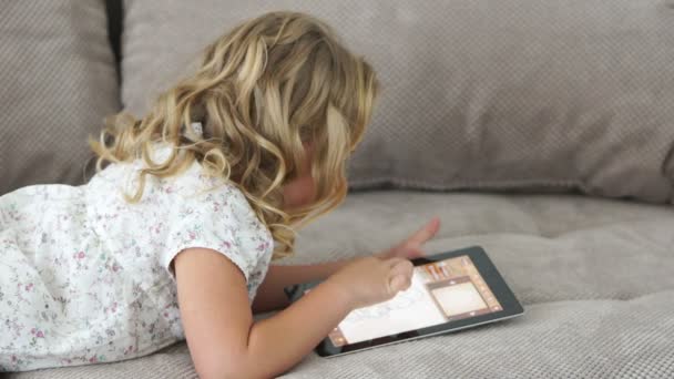 Liten flicka på soffa spelar på TabletPC — Stockvideo