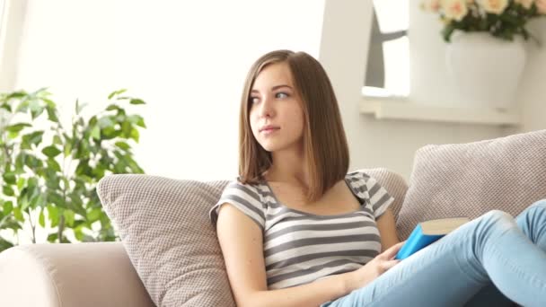 Chica sentada en el sofá con libro — Vídeos de Stock