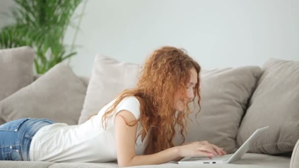 Mujer relajante en el sofá utilizando el ordenador portátil — Vídeo de stock