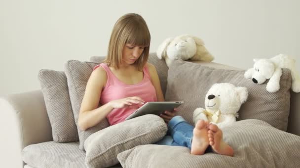 Девушка сидит на диване с планшетом — стоковое видео