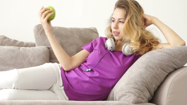 Chica acostada en sofá comer manzana — Vídeos de Stock