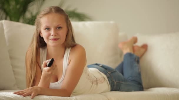 Дівчина розслабляється на дивані тримає пульт дистанційного керування — стокове відео
