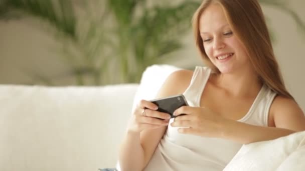 Chica sentada en el sofá usando el teléfono — Vídeos de Stock