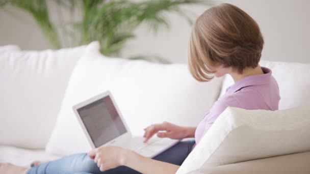 Жінка сидить на дивані за допомогою ноутбука — стокове відео