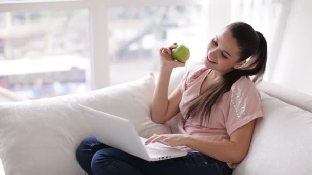 Woman sitting on sofa eating apple — Stock Video