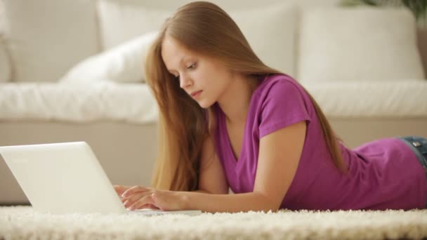 Chica acostada en la alfombra utilizando el ordenador portátil — Vídeos de Stock