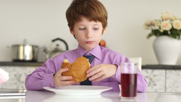 Niño sentado a la mesa comiendo hamburguesa — Vídeos de Stock