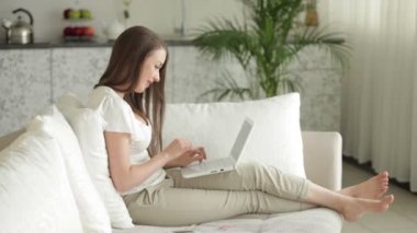 Kanepede dizüstü bilgisayarlı bir kadın oturuyor.