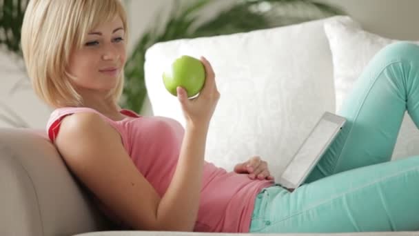 Mujer en el sofá usando touchpad comer manzana — Vídeo de stock