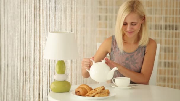 Девушка сидит в кафе наливая чашку в чай — стоковое видео