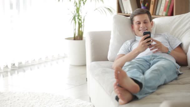 Hombre acostado en un sofá con teléfono celular — Vídeos de Stock