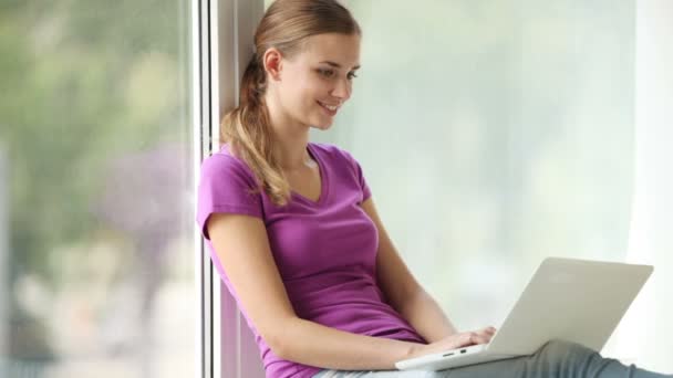 Girl sitting by window using laptop — Stock Video