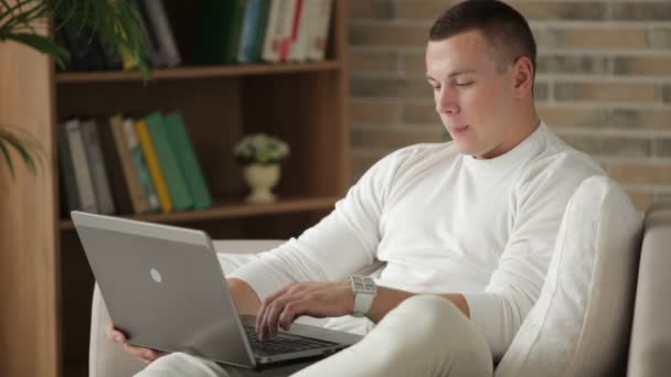 Chlapík sedí na gauči, přes notebook — Stock video