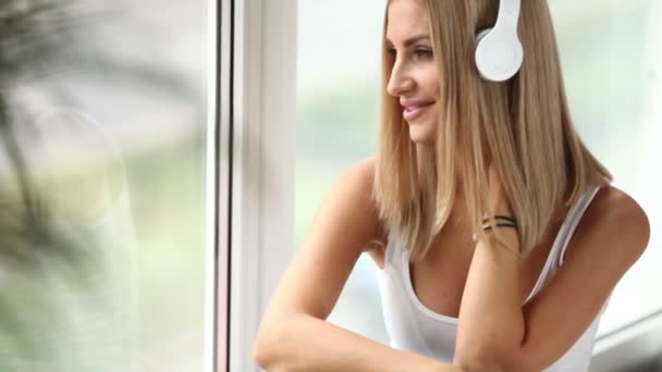 Девушка, сидящая у окна, слушая музыку — стоковое видео