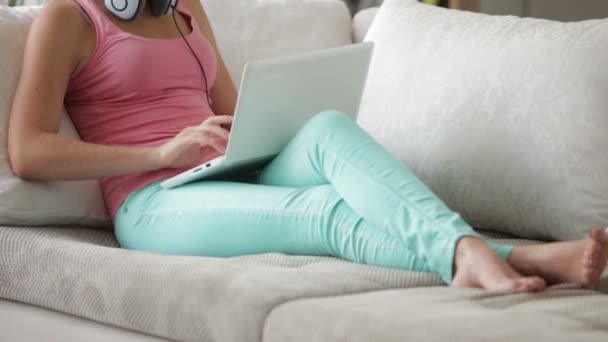 Frau trägt Kopfhörer auf Sofa mit Laptop — Stockvideo