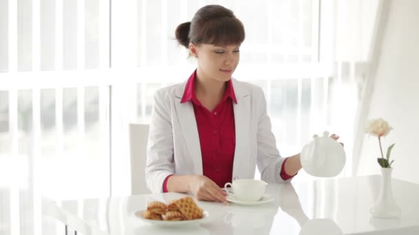 Meisje zitten aan tafel en gieten thee — Stockvideo