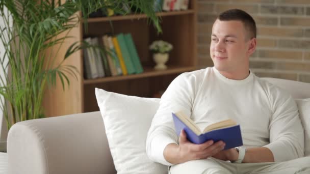 Hombre sentado en el sofá con libro — Vídeos de Stock