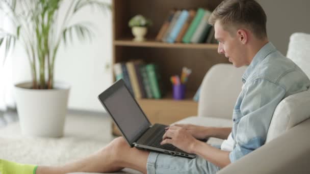 Tipo sentado en el sofá y el uso de ordenador portátil — Vídeos de Stock