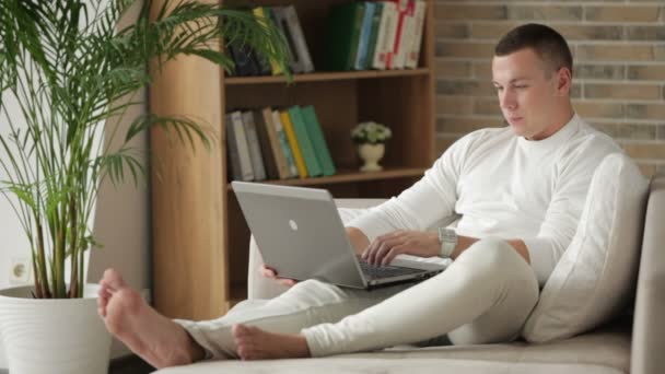 Man sitter på soffan med laptop — Stockvideo