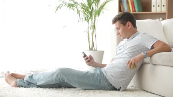 Человек, сидящий на ковре с помощью мобильного телефона — стоковое видео